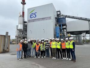 Groupe d’élèves ingénieurs, portant casques et chasubles fluos, posant devant une centrale de production électrique arborant le logo Électricité de Strasbourg.