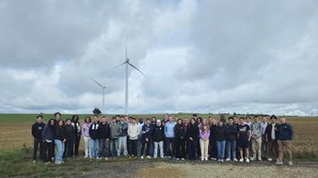 Groupe d'élèves ingénieurs posant devant un parc éolien lors de leur visite sur la Route des Énergies Renouvelables.