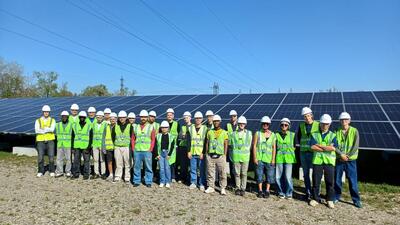 Premier groupe de visite posant avec leur casque et leur gilet fluo devant un champ de panneaux solaires